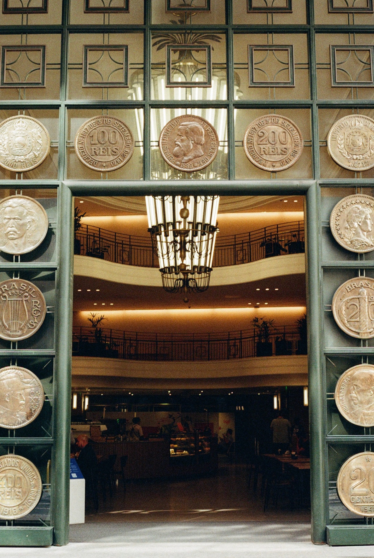Ornate green metal doorway framed by giant Brazilian coin reliefs at the Casa da Moeda hall
