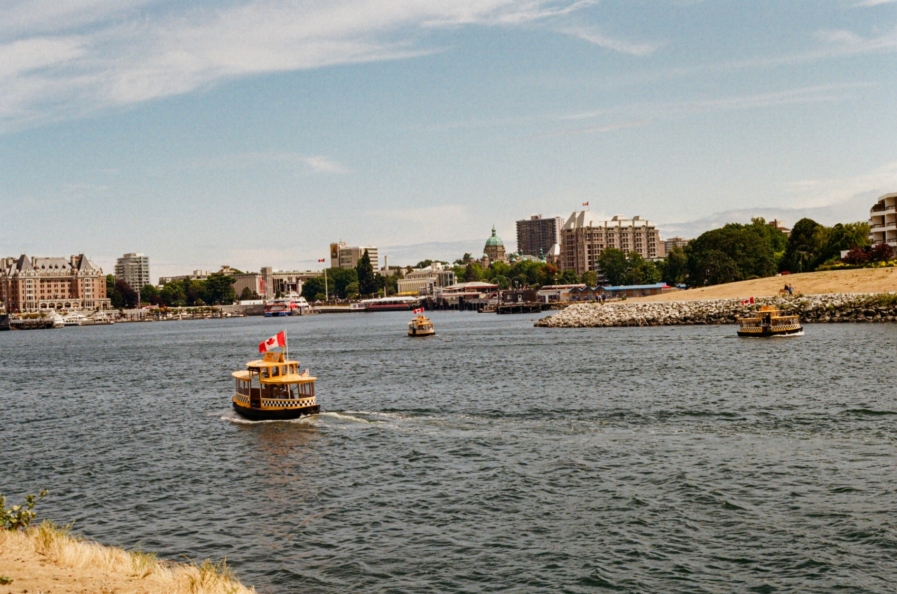 Yellow harbor taxi boats with Canadian flags cross Victoria's Inner Harbour with the Parliament dome behind