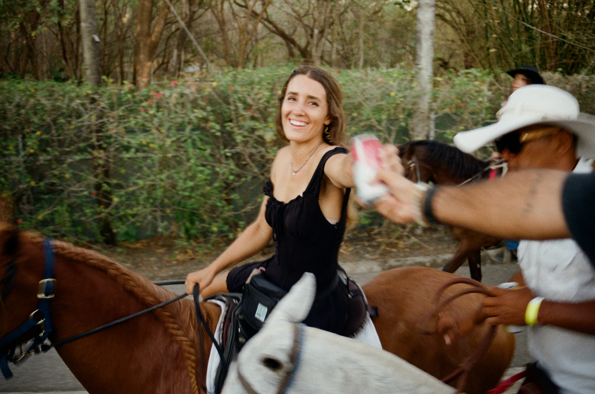 Woman in a black dress smiling while horseback riding through a tropical trail in Costa Rica