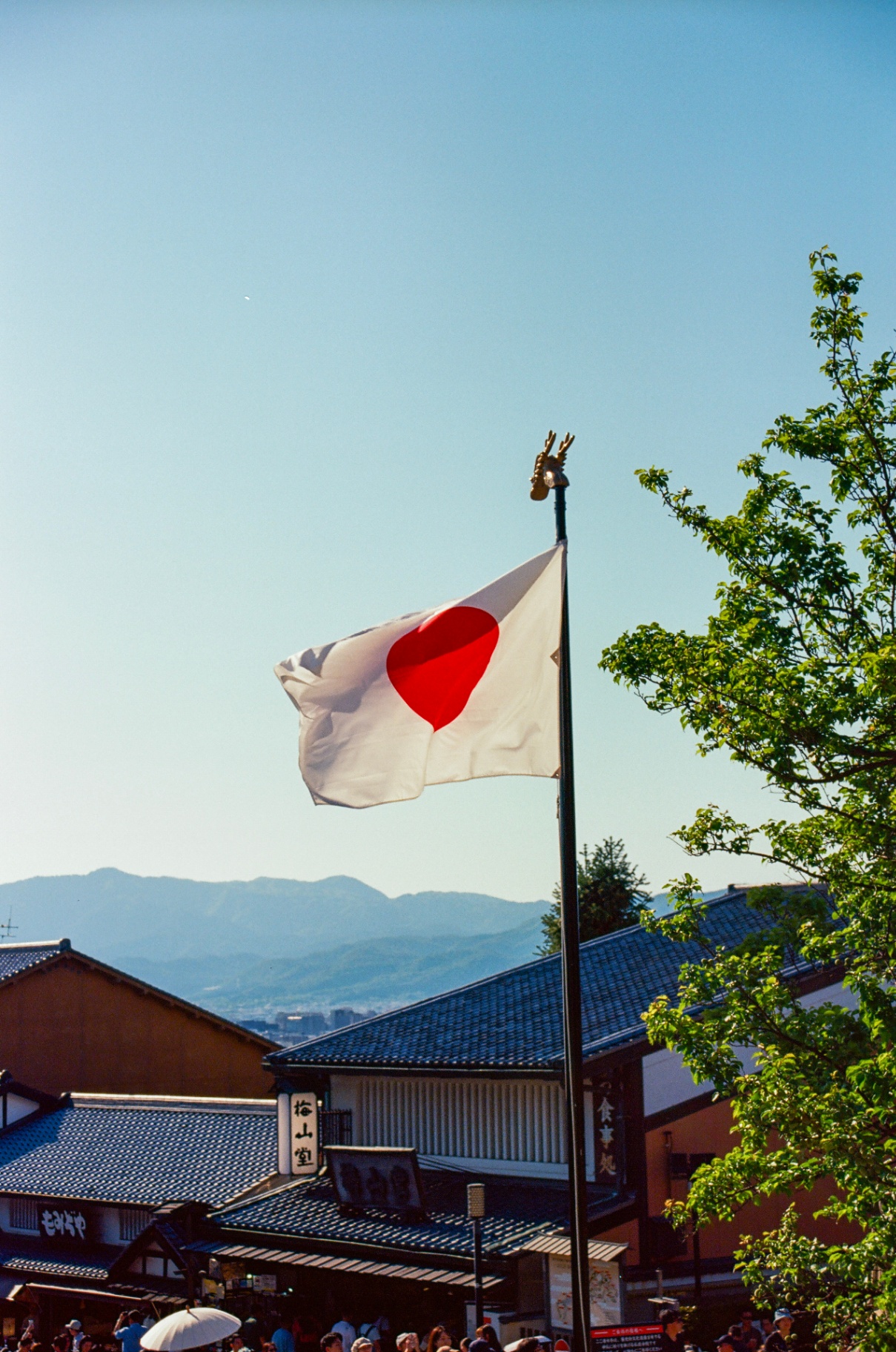 Japanese flag flying above tiled rooftops with mountains in the distance, Kyoto