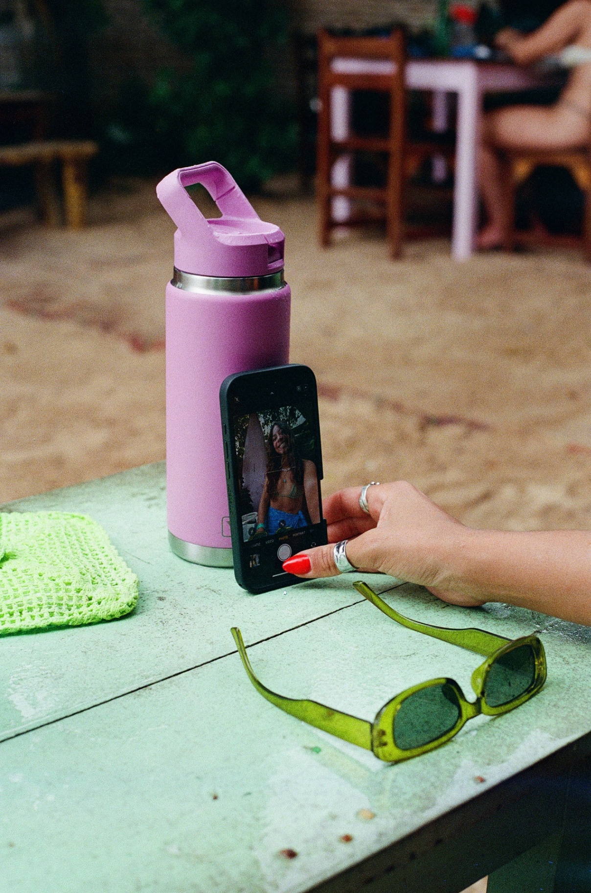 Pink bottle and green sunglasses on a beach table