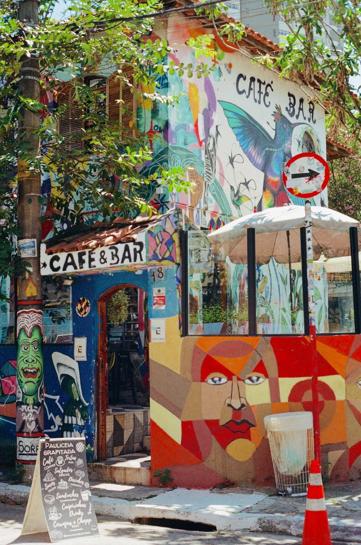Colorful mural-covered Café & Bar on a São Paulo corner surrounded by trees
