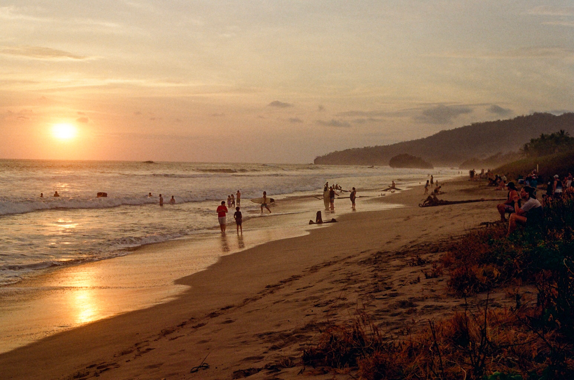 Surfers and beachgoers gathered on a Costa Rica beach as the sun sets over the ocean