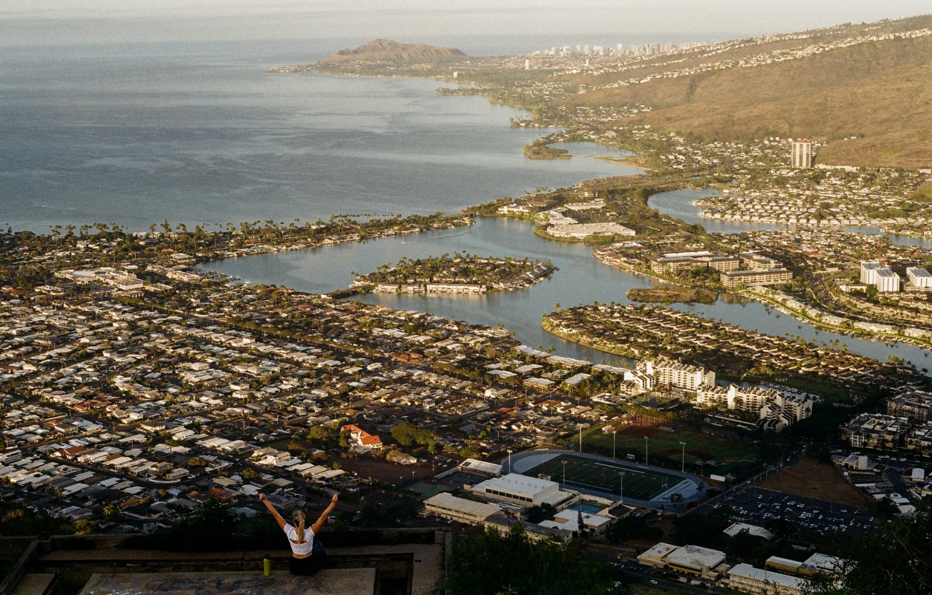 Woman with arms raised on the Koko Head summit overlooking Hawaii Kai and the coastline