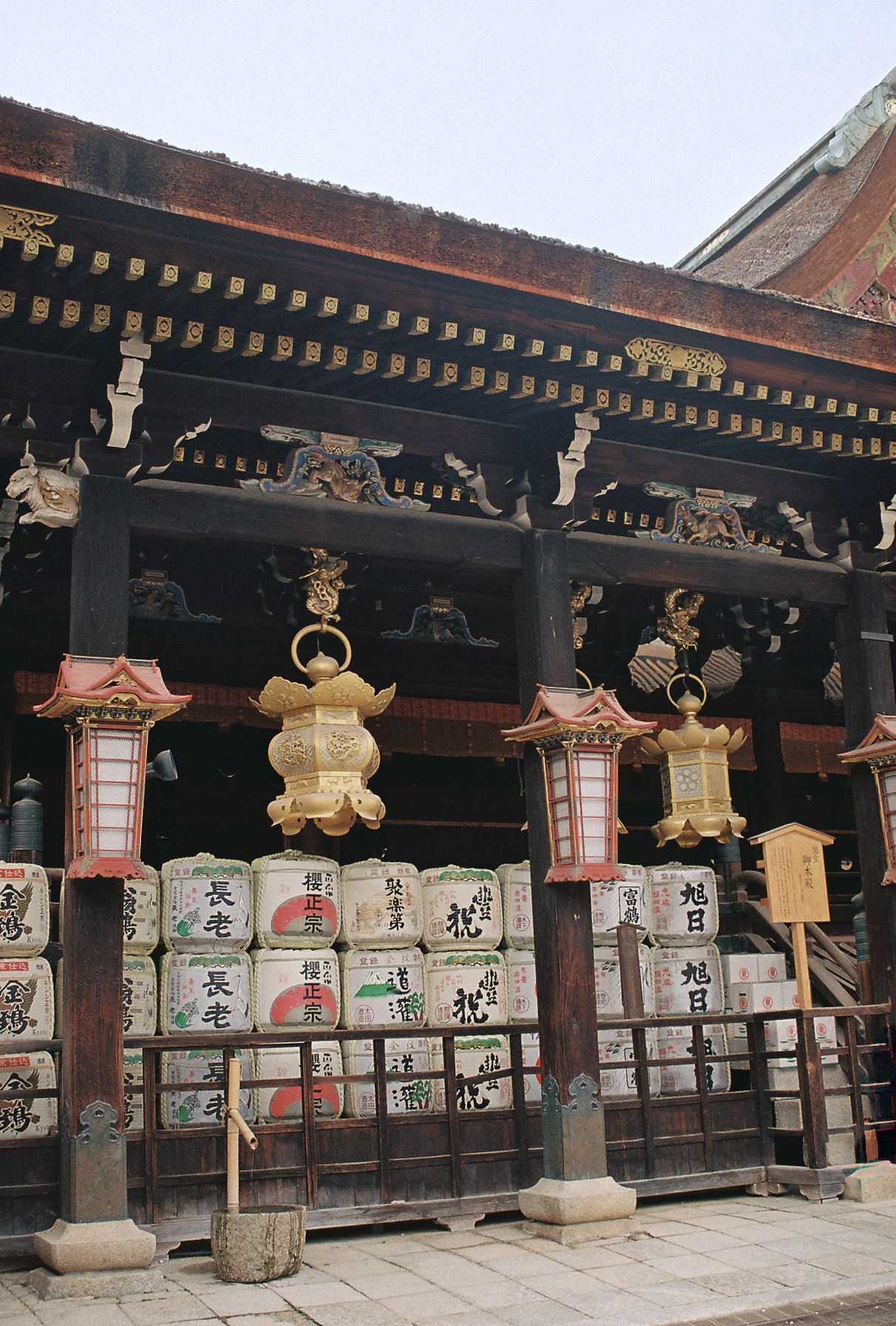 Stacked sake barrels and hanging lanterns beneath the eaves of a Kyoto shrine