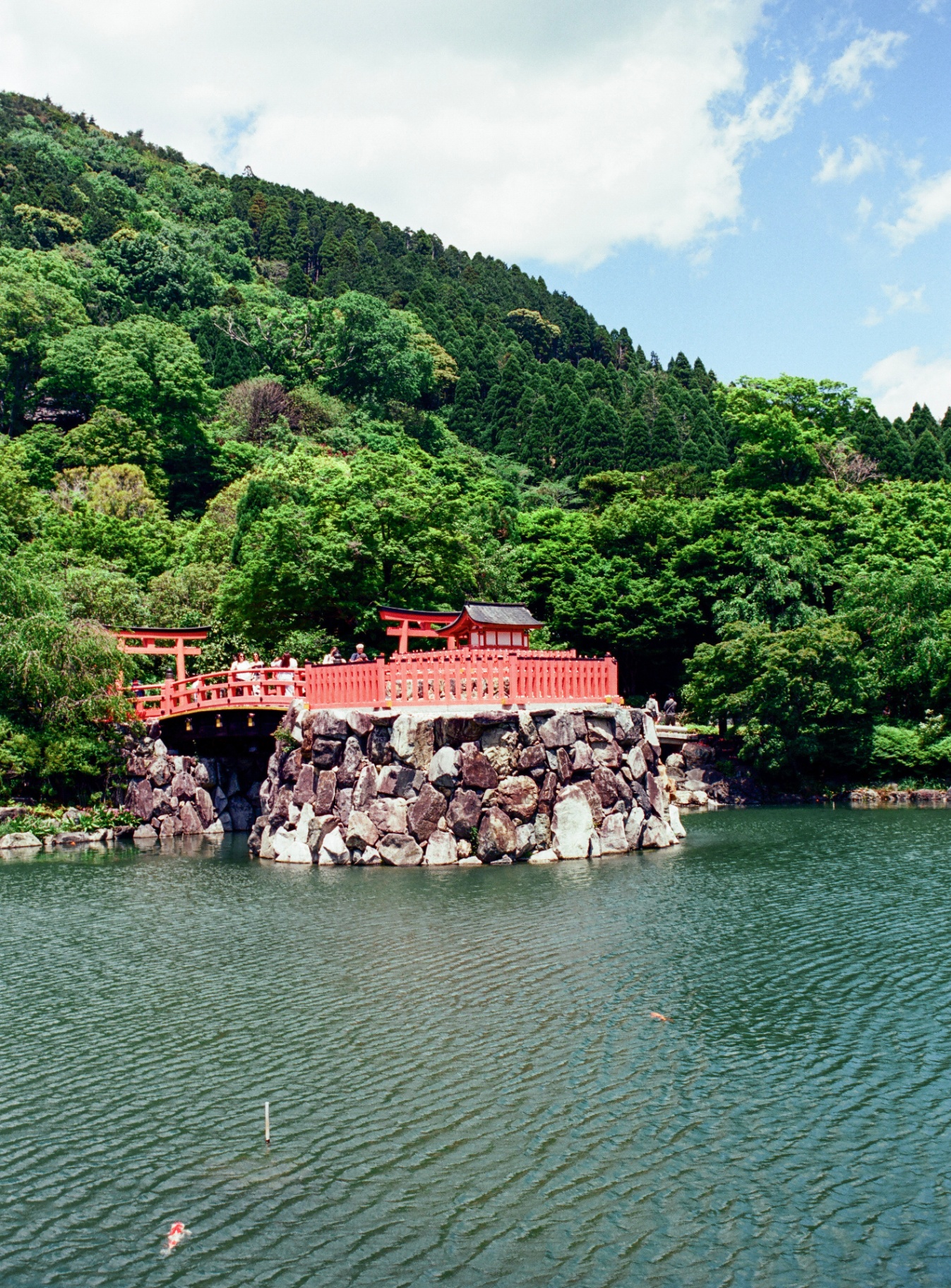 Red bridge and small torii on a stone island in a Hakone lake, surrounded by green mountains