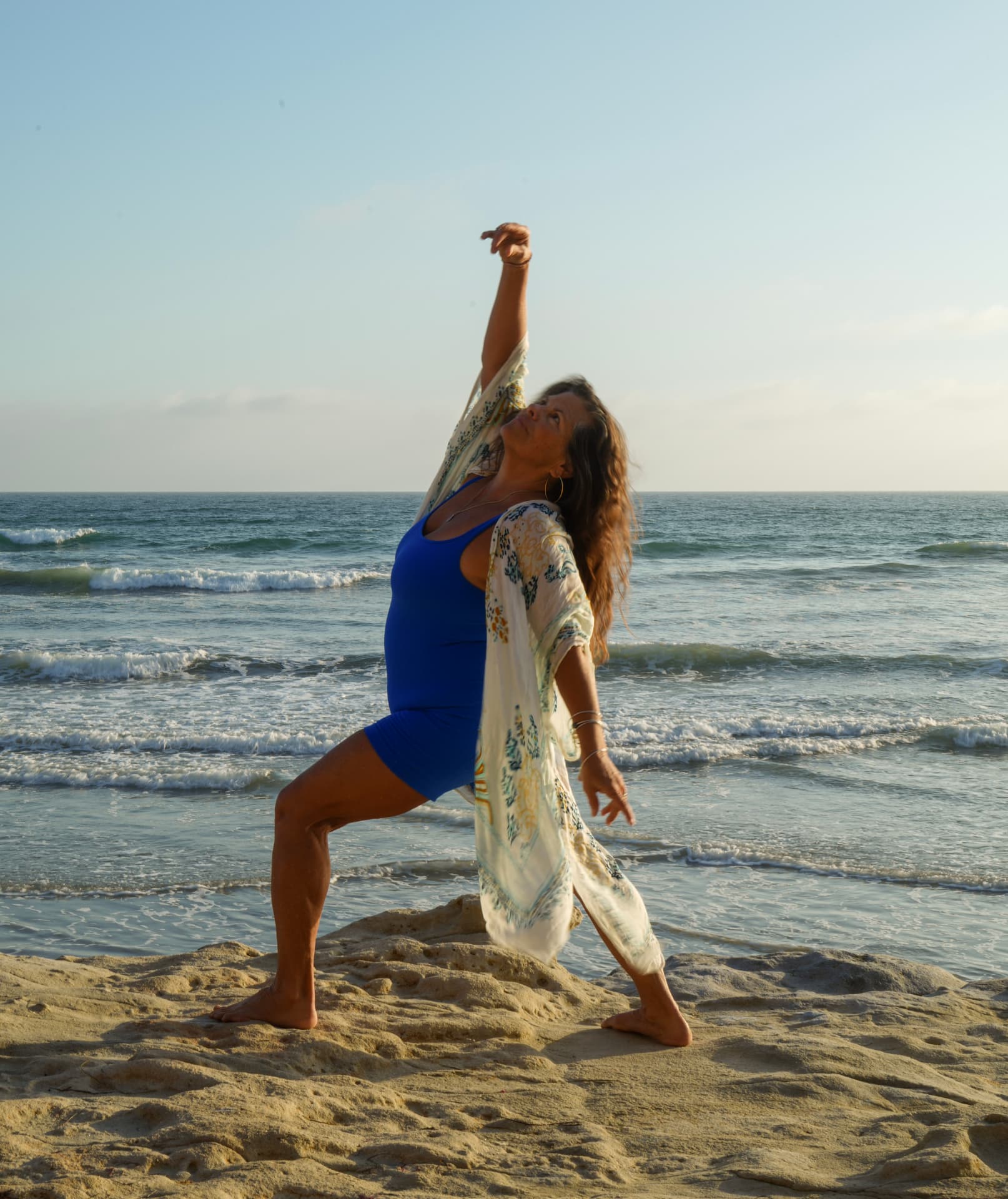 Dancer in blue on coastal rocks beside the pale blue ocean