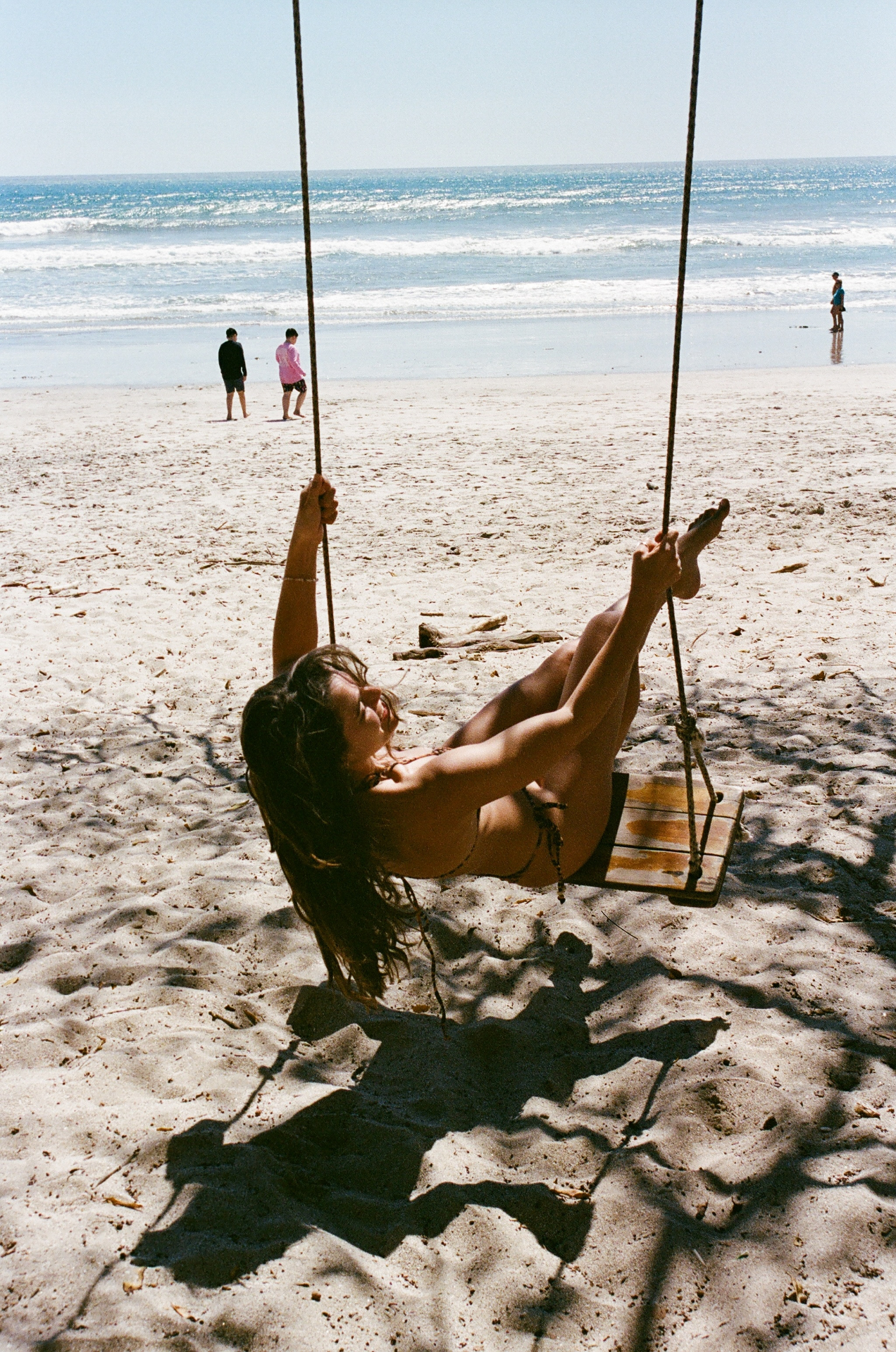 Woman reclining on a wooden swing under shade on a bright Costa Rica beach