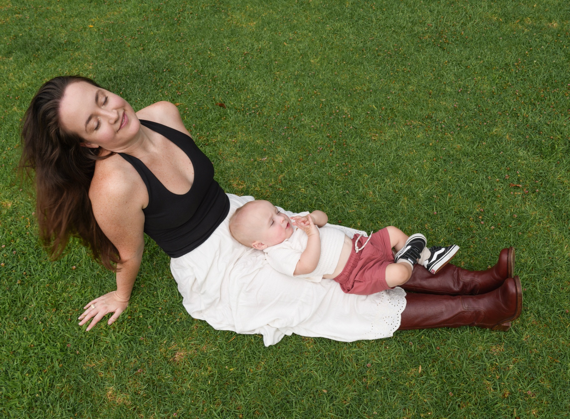 Overhead of a mother sitting on the grass with her baby resting on her lap