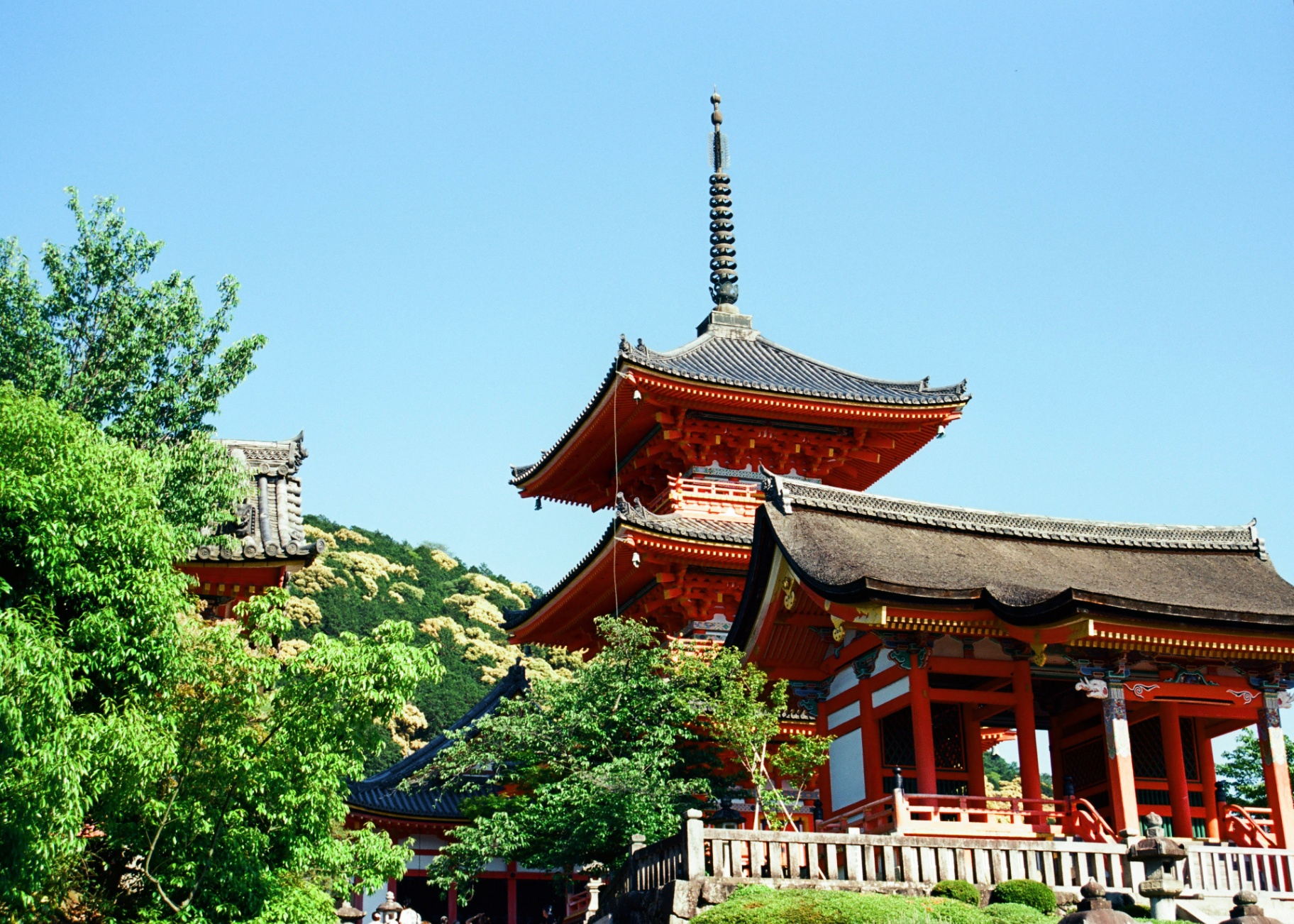 Vermilion pagoda and gate of Kiyomizu-dera temple framed by trees in Kyoto