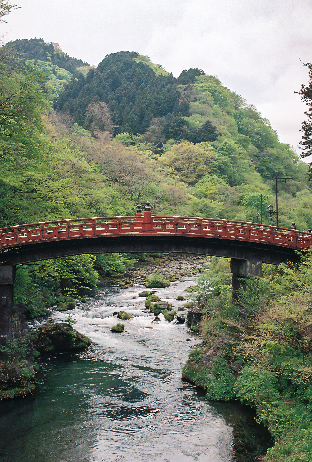The red Shinkyo bridge over a rushing river in the green mountains of Nikko