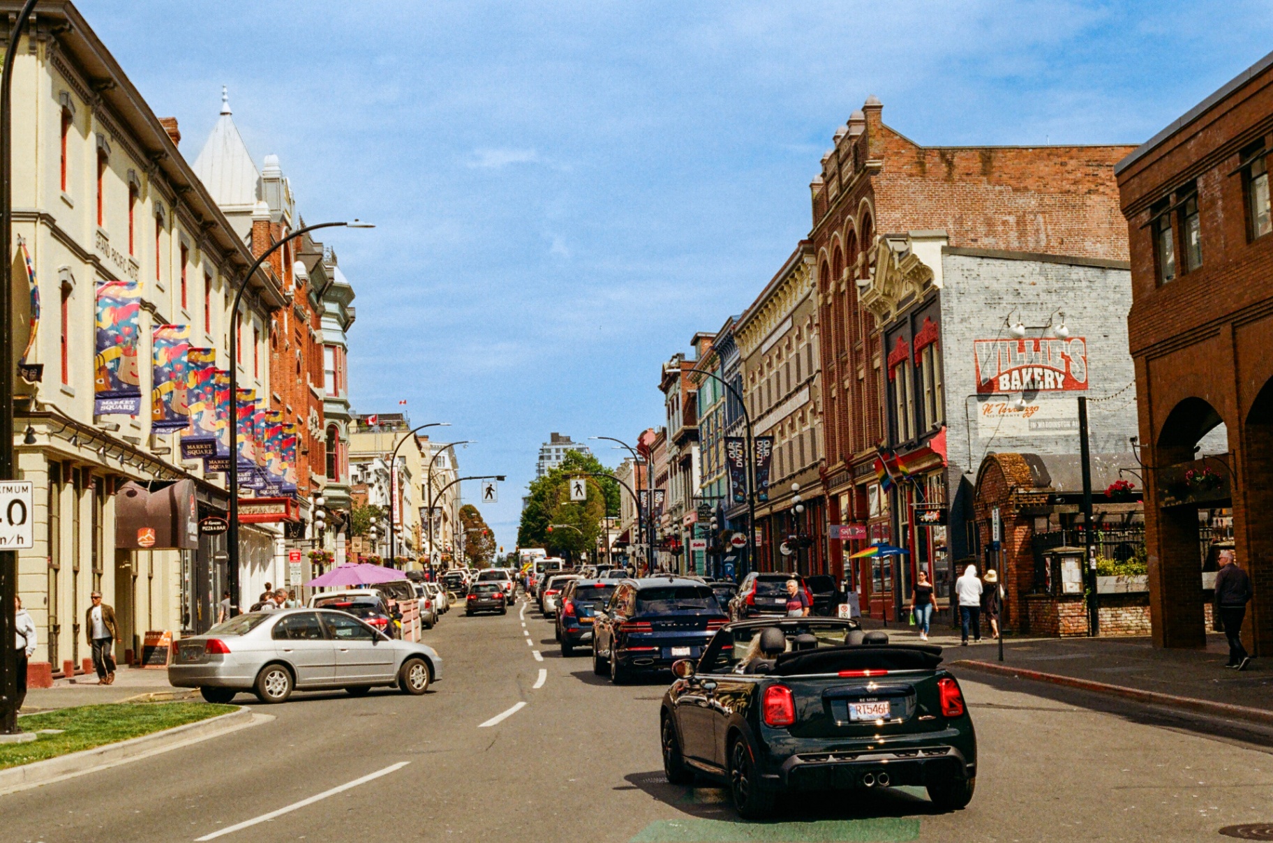 Downtown Victoria street with historic brick facades, banners, and a convertible mini in traffic