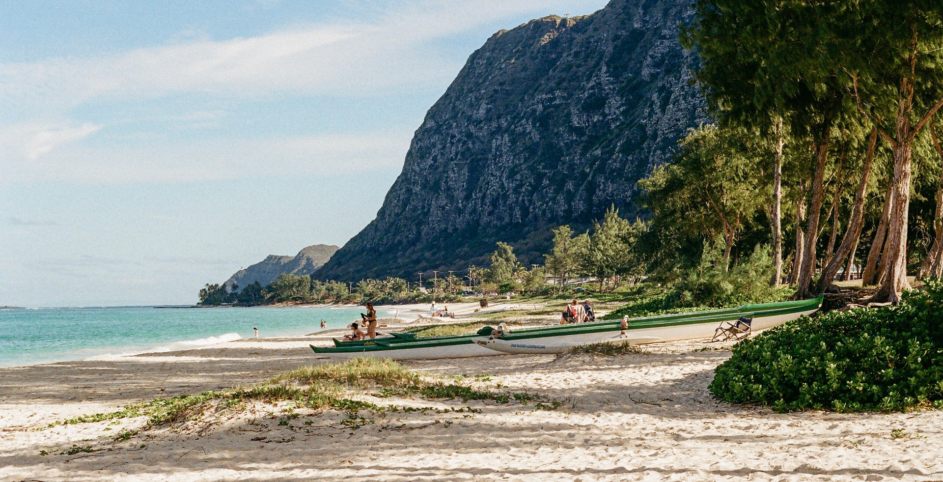 Outrigger canoes resting on Waimanalo Beach beneath a dramatic mountain ridge