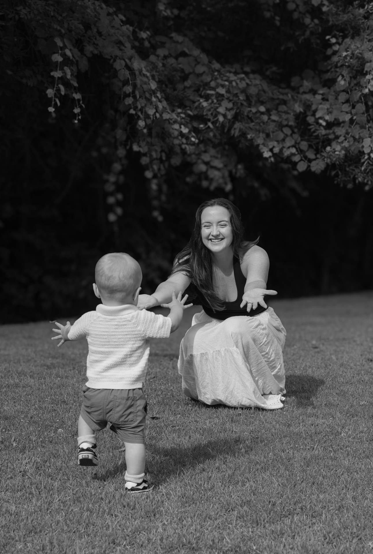 Baby running into mother's open arms on the grass, black and white