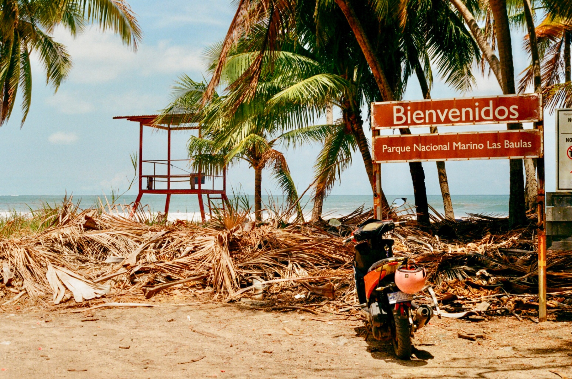 Bienvenidos sign for Parque Nacional Marino Las Baulas with a red lifeguard tower and palm trees