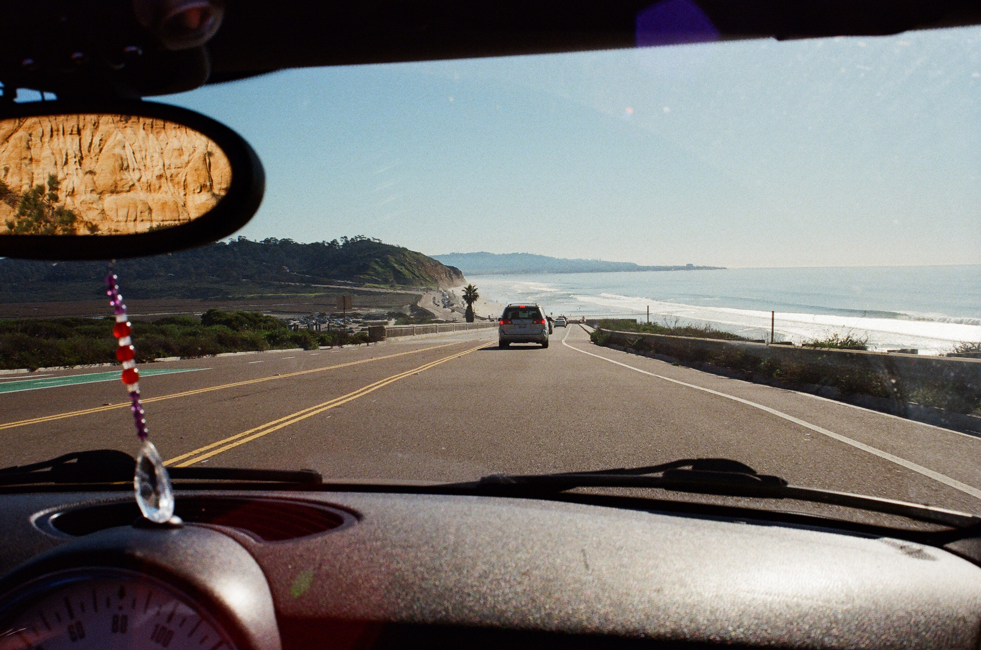 View from a car windshield driving the Pacific Coast Highway with Torrey Pines cliffs and ocean to the right