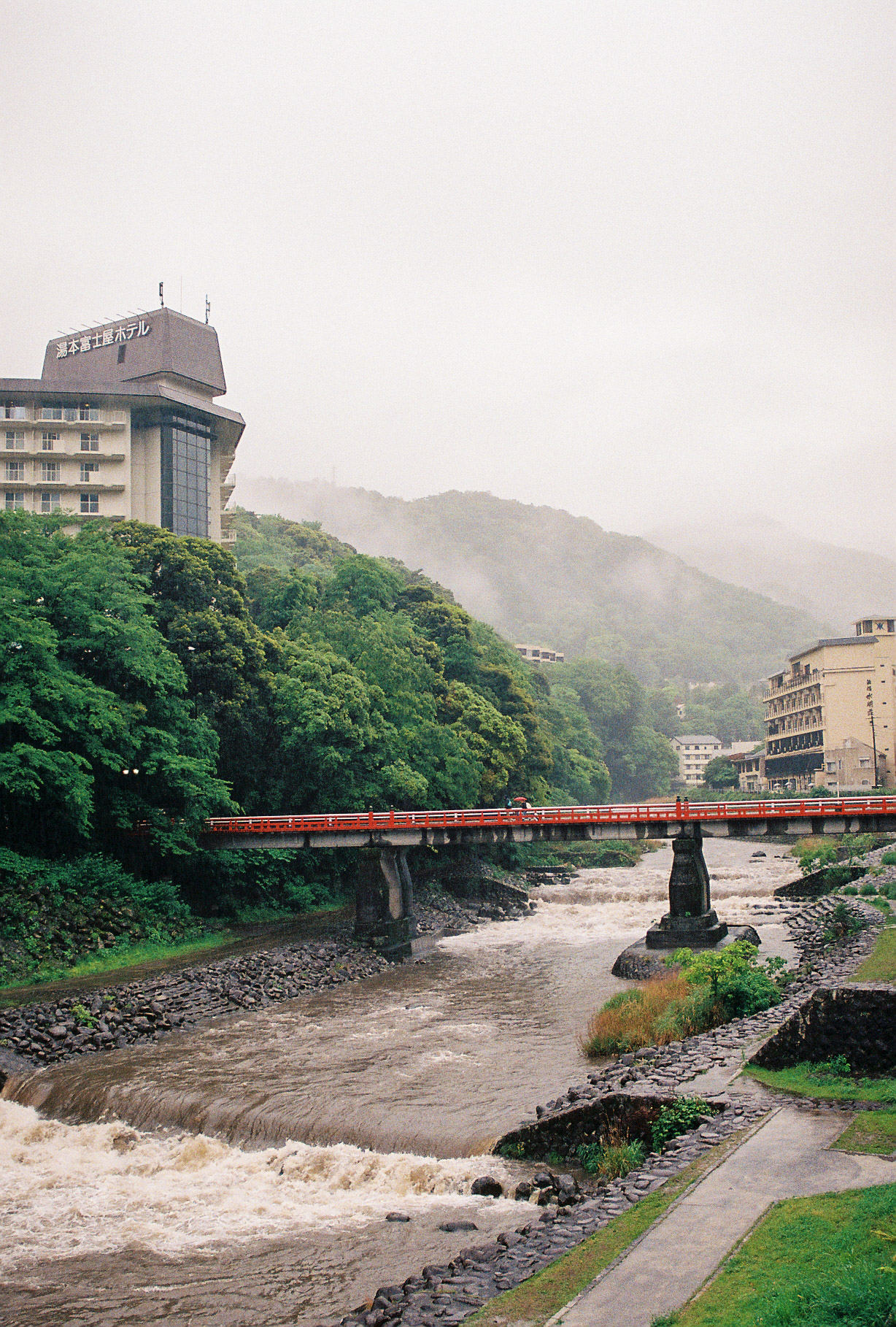 A red bridge over a swollen river in Hakone on a misty rainy day
