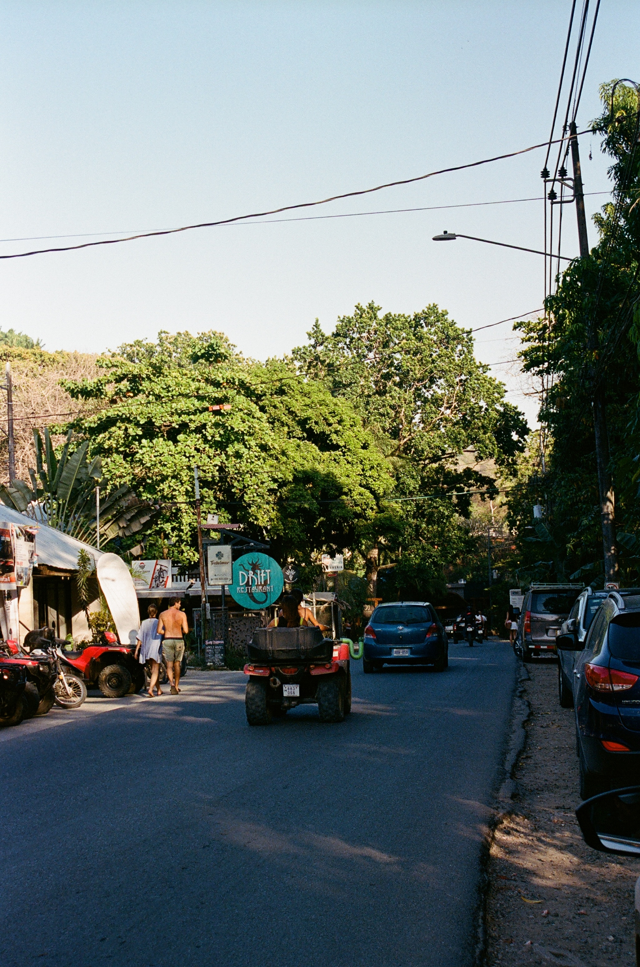 A quiet Costa Rica street with cars, an ATV, and a turquoise Drift Restaurant sign