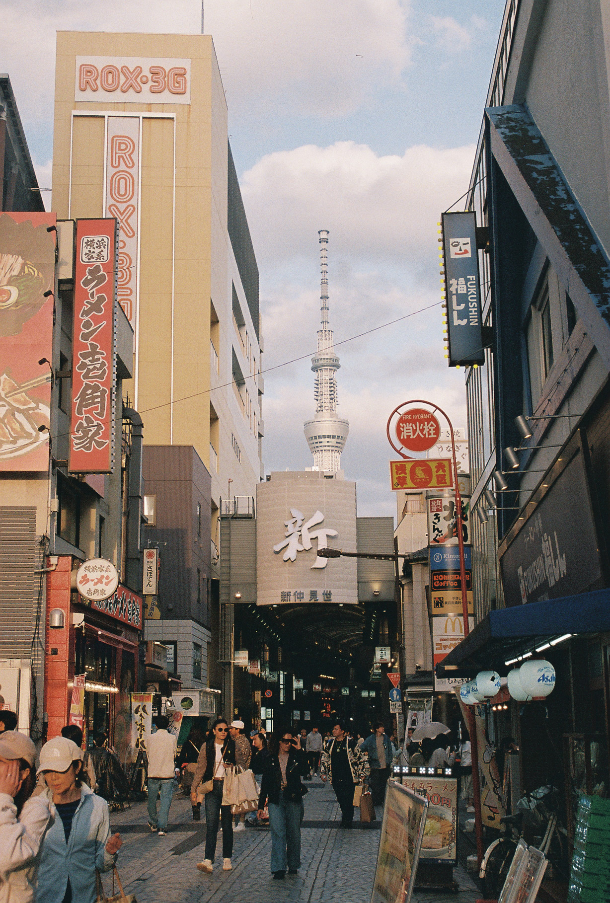 Tokyo Skytree rising above a busy Asakusa shopping street with ROX-3G signage