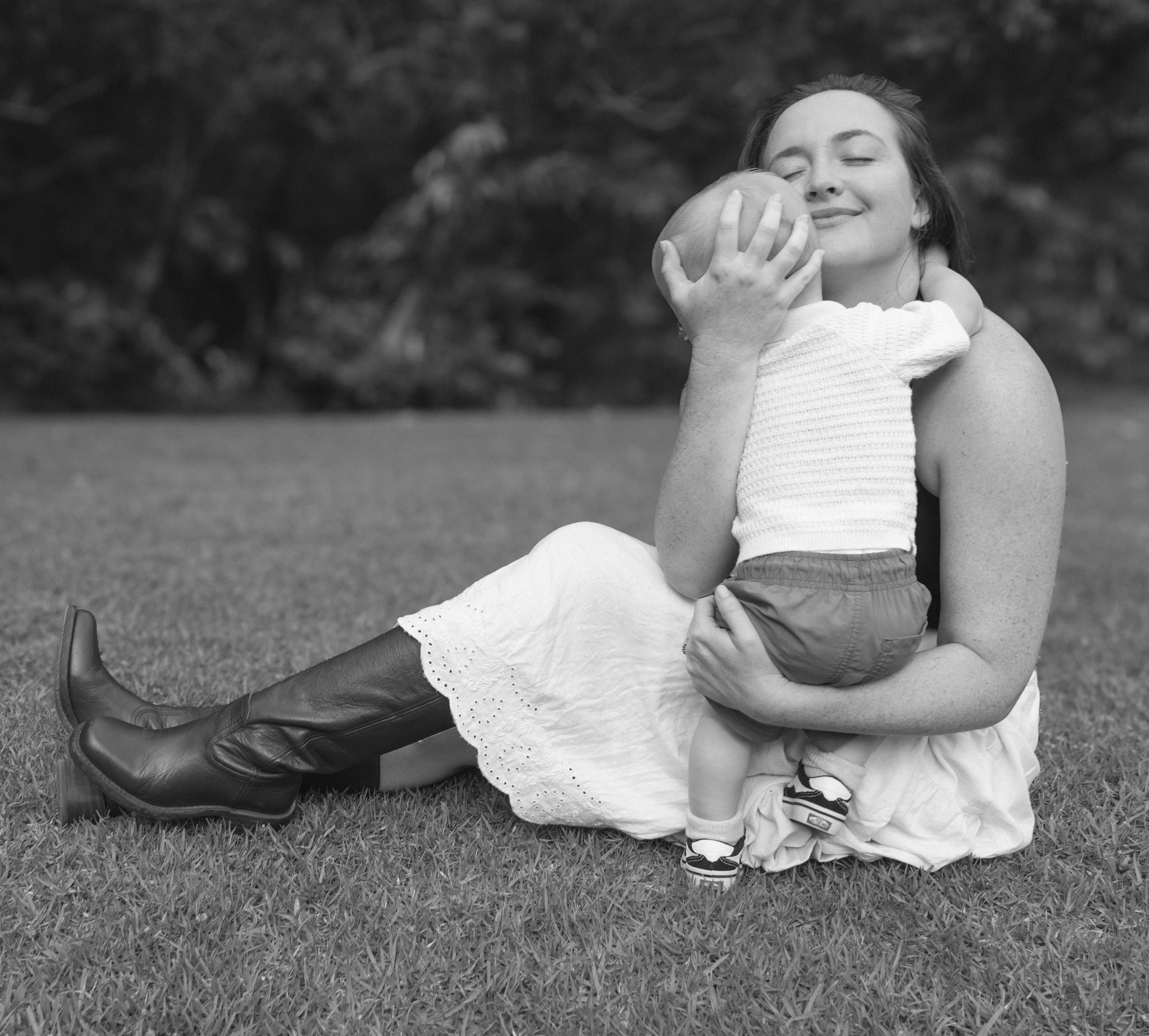 Mother sitting in the grass holding her baby close, black and white