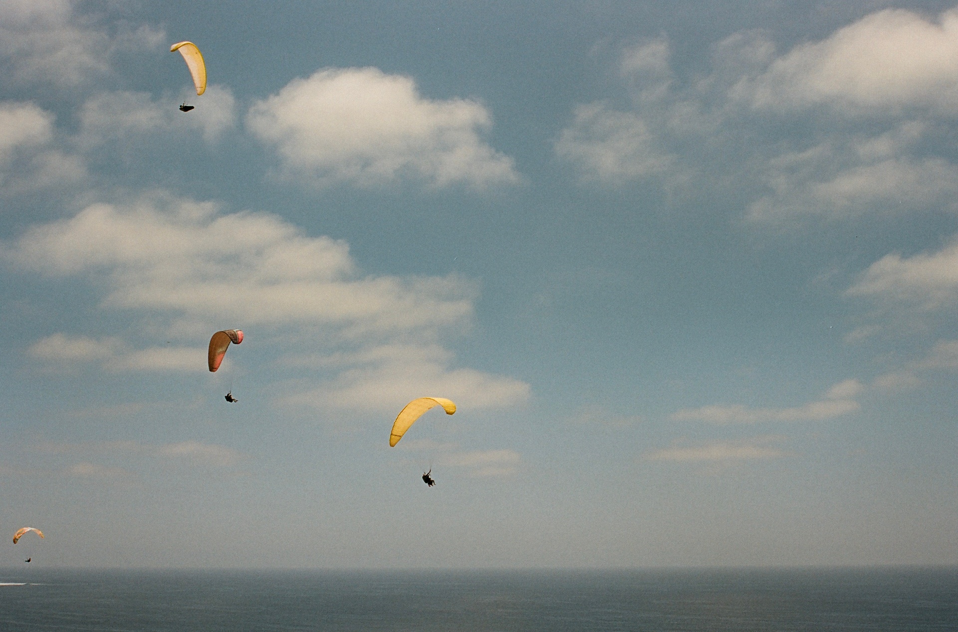 Yellow and orange paragliders drifting through a cloud-flecked sky above the Pacific at Torrey Pines