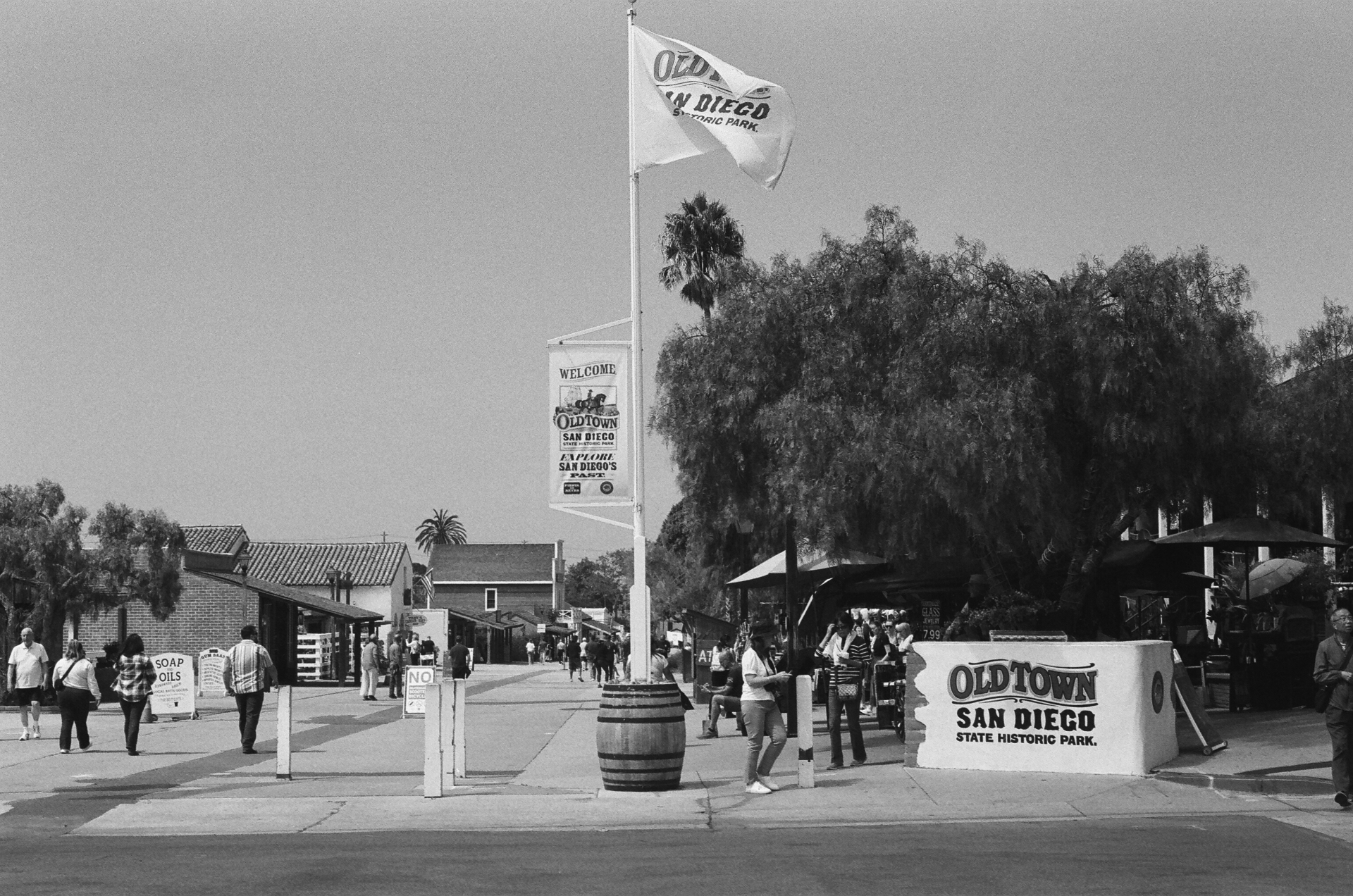 Black and white photo of the Old Town San Diego State Historic Park entrance with flag and palm trees