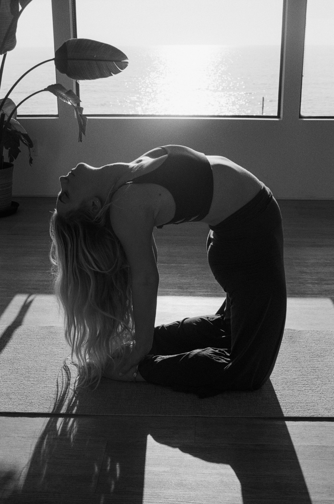 Black-and-white yoga backbend beside an ocean-view window