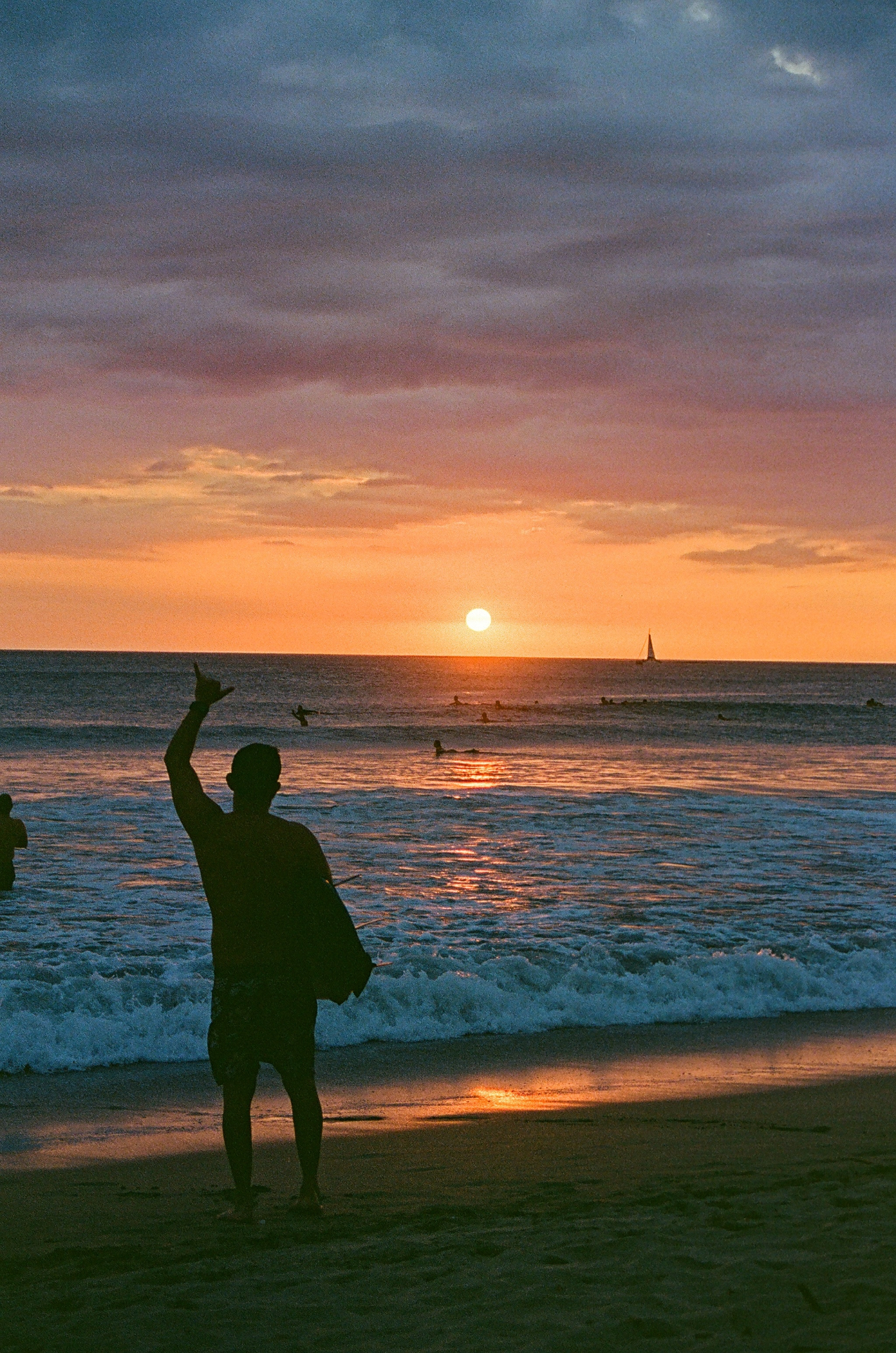 Silhouette of a person at sunset on a Costa Rica beach with surfers and a sailboat offshore