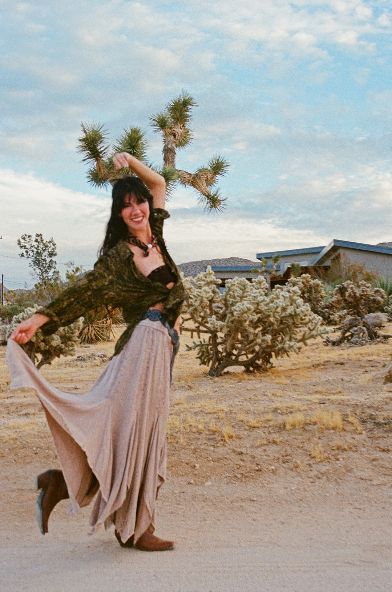 Smiling in a desert clearing, lifting the hem of a long skirt beneath a Joshua tree