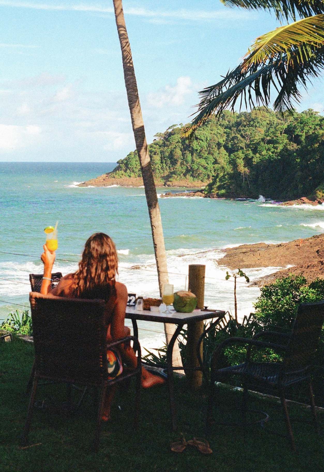 A woman holding a tropical drink overlooking the ocean in Brazil