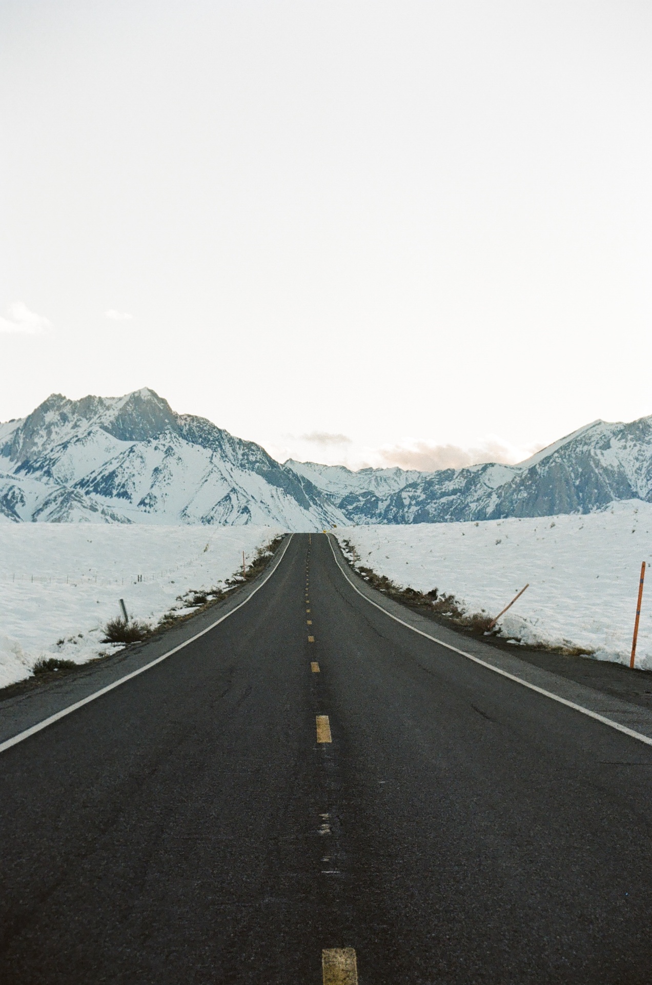 Empty road leading toward snow-covered Eastern Sierra peaks at dusk