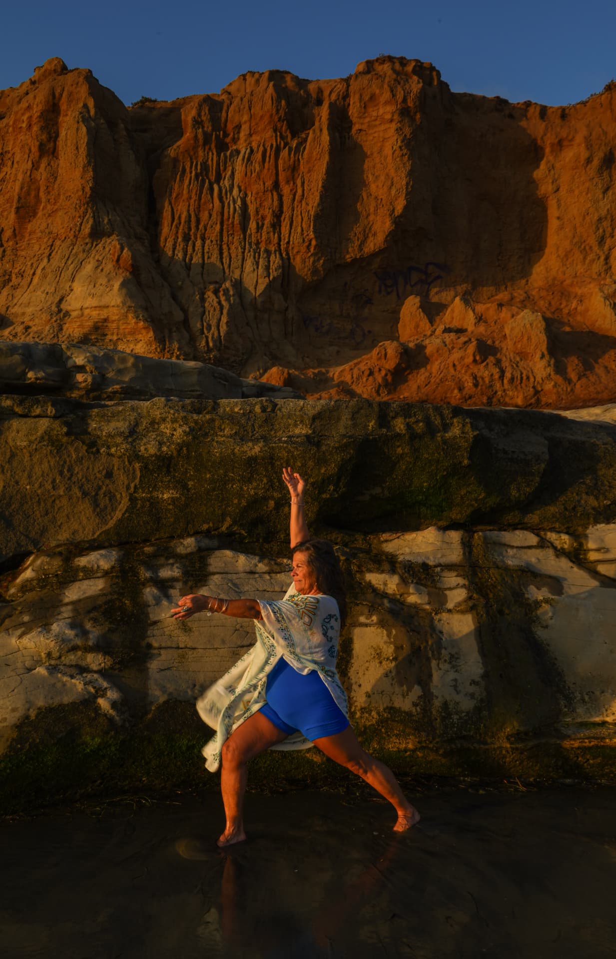 Dancer beneath terracotta cliffs in golden evening light