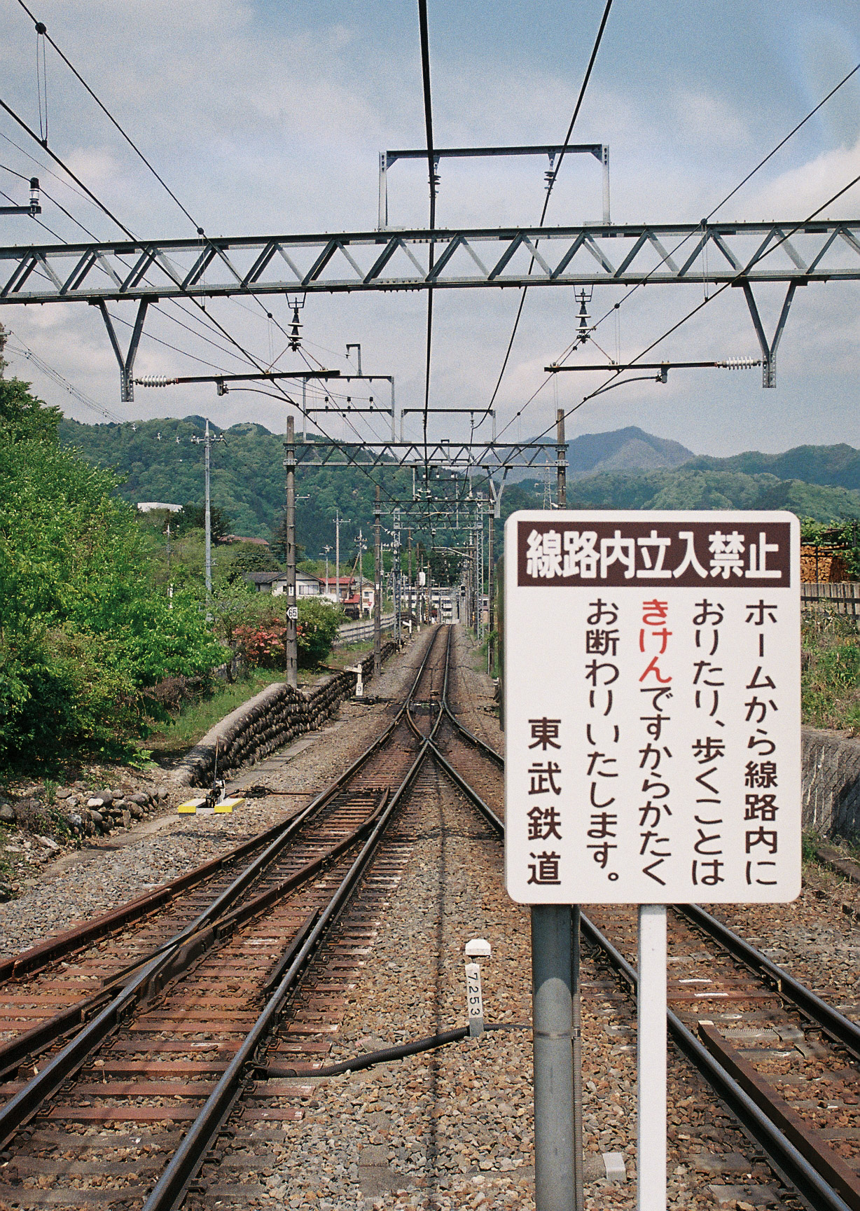Tobu railway tracks heading into the mountains with a Japanese warning sign in the foreground