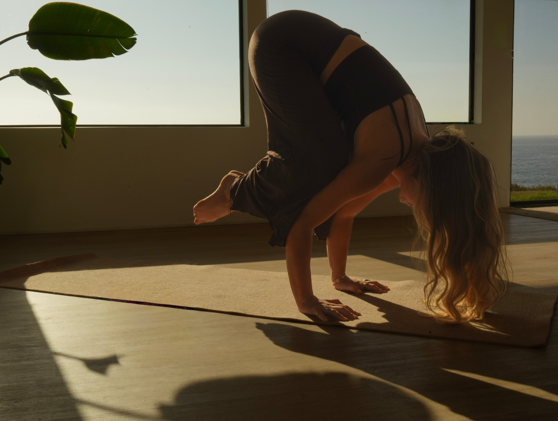 Yoga arm balance beside an ocean-view window in warm sunlight